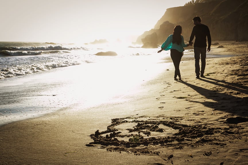 Jenn and Peter hold hands as they walk together on the beach